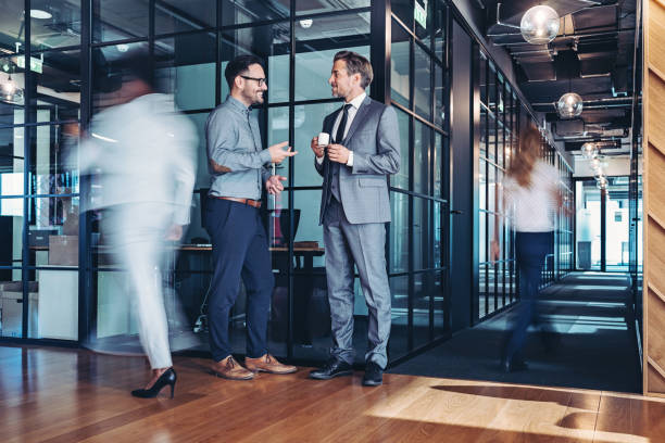 istock Two businessmen having a conversation in a modern office space with other people walking around in a blurred motion 2201300937