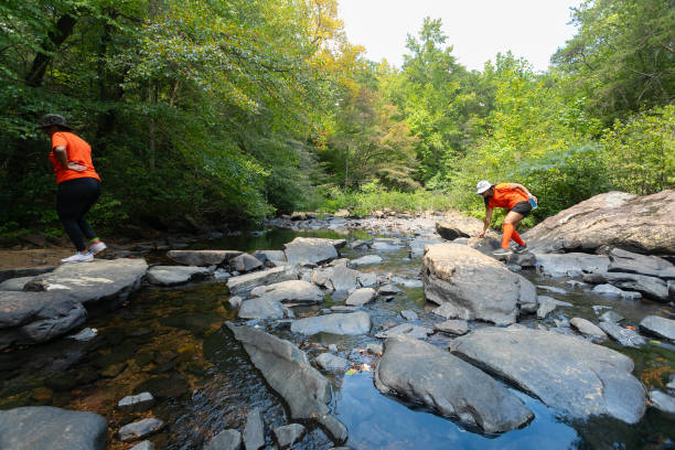 Women crossing rocking riverbed while hiking out in the mountains in Tennessee on a beautiful day