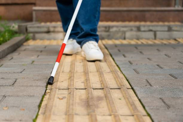 istock A blind woman walks outdoors using a cane along a tactile yellow tile. 2201310760