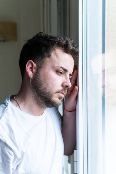 istock Sad young man leaning his head against window at home 2201316373