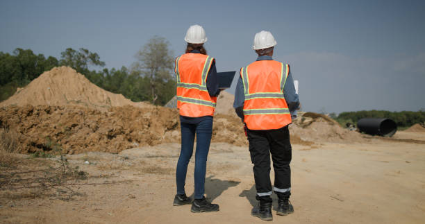 istock The project engineer team with orange safety vests  holds laptops and blueprint drawings working at the construction sideline, drainage construction 2201324511