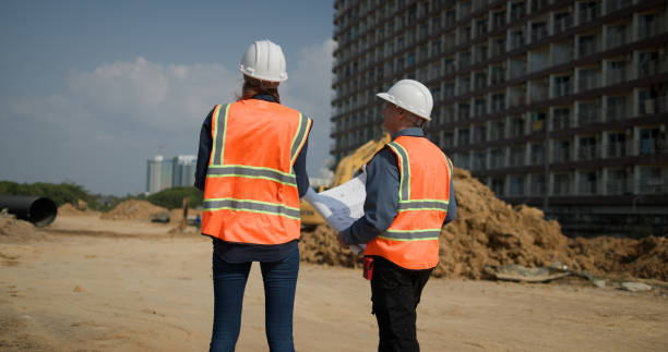 istock The project engineer team with orange safety vests  holds laptops and blueprint drawings working at the construction sideline, drainage construction 2201324519