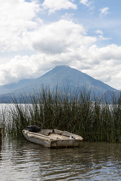 An old and possibly abandoned craft hiding at peaceful, calm Lake Atitlan at Santa Catarina, Palopo, Guatemala. Volcanoes in the background.  Full frame, no people. Part of a series.