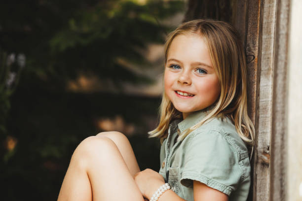 A beautiful, little girl, 8 years old,  smiles at the camera as she sits on a rustic porch. Shot with a Canon 5D Mark IV.