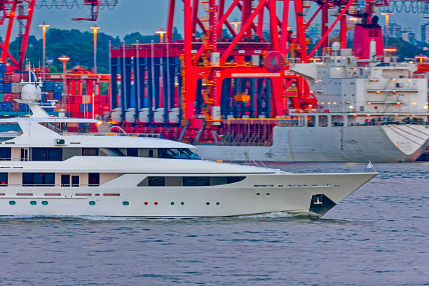 Yacht passing by a container ship docked in the Vancouver Burrard Inlet harbor, British Columbia