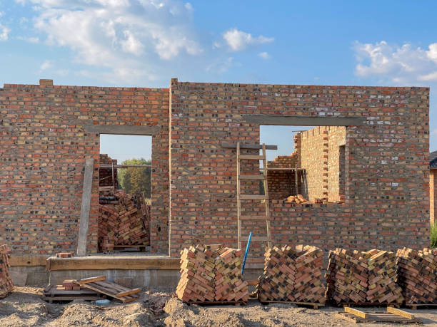 istock A brick structure is taking shape with open windows and a ladder leaning against the wall, surrounded by piles of bricks on a construction site in bright daylight 2201363518
