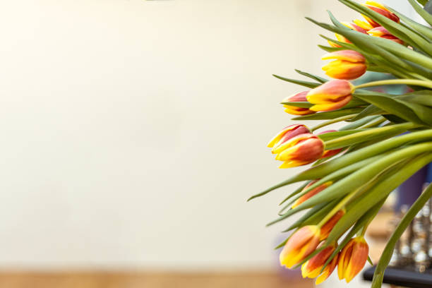 A bouquet of vibrant yellow and orange tulips is elegantly displayed on a table, brightening the indoor space with their cheerful colors during the spring season.