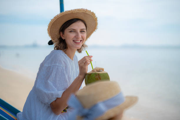 Woman enjoying coconut water while relaxing on the beach with family in a tropical setting