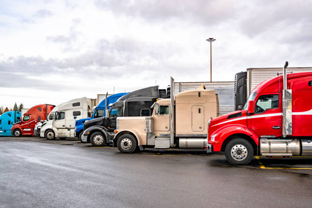 istock Different makes and models of the big rig semi trucks with semi trailers standing in row on truck stop parking lot take a break 2201405234