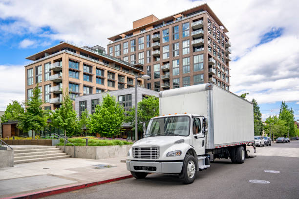 Popular local delivery and moving day cab middle duty semi truck with box trailer standing on the urban city street with multilevel apartment building unloading delivered goods stock photo