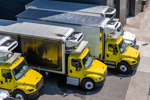 Yellow and white middle duty day cab rigs semi trucks with refrigerated box trailers standing in row on the industrial parking lot waiting for the next local deliveries stock photo