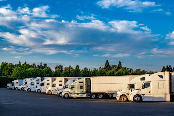 istock White different big rig semi trucks with semi trailers standing in row on truck stop parking lot at sunny day with clouds sky 2201405680