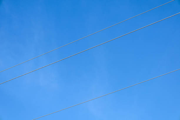 Two power lines are shown stretching horizontally across the frame against a bright blue sky. The lines are thin, dark in color, clearly distinguishable against the sky.