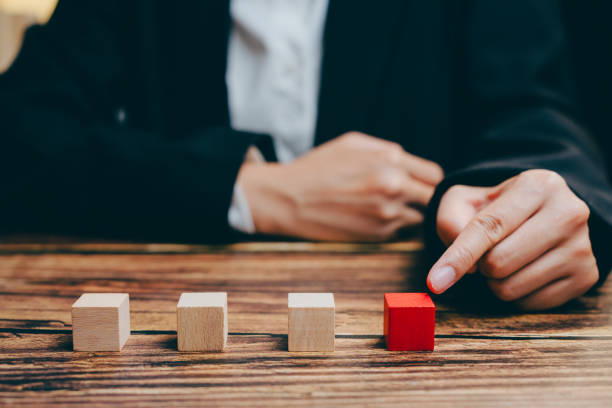 istock Person Pointing at Red Cube Among Wooden Cubes on Table, business concept 2201413427