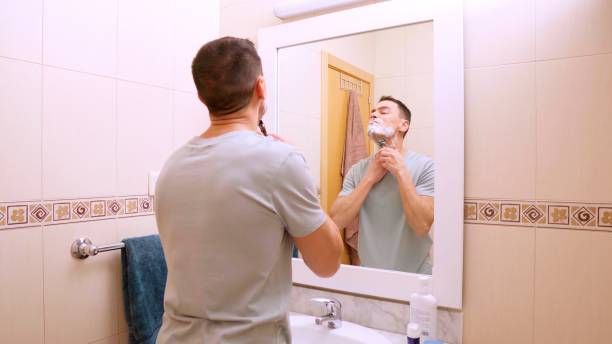 istock Man shaving his beard in bathroom mirror 2201421634