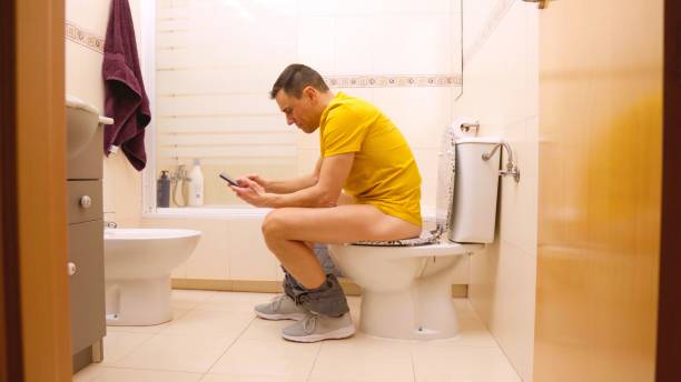 istock Man sitting on toilet using smartphone in bathroom 2201422017
