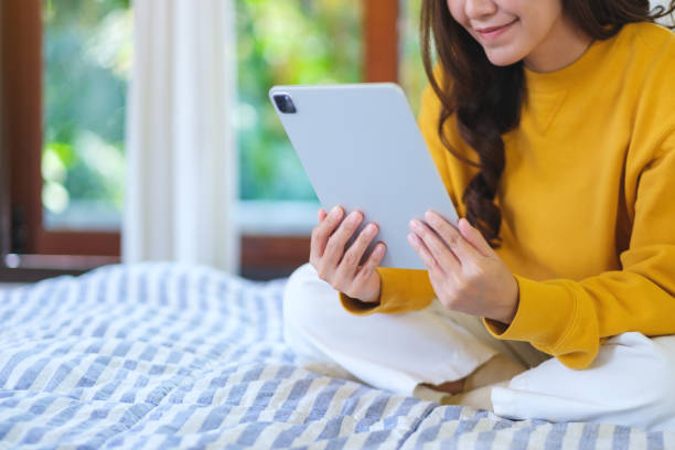 Closeup of a woman holding and using Apple New Ipad Pro digital tablet while sitting on bed