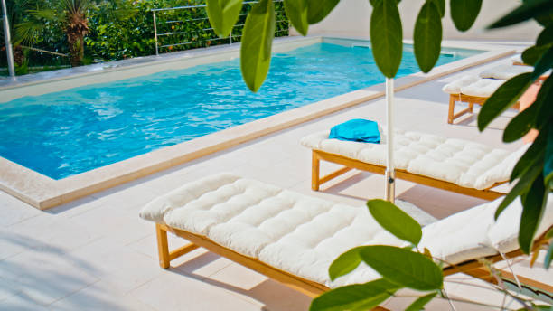A serene resort pool with crystal-clear water, sunlit loungers in white cushions, and lush tropical greenery, evoking a tranquil summer retreat.