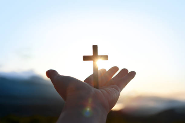 istock Christian's hands stretched out toward the rising sun, brilliant light shining through the cross of Jesus Christ, faith and belief background 2201433907