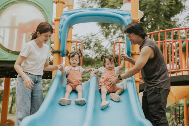 istock Smiles and Support: Bonding of Parents Assist Twins on a Slide 2201434224