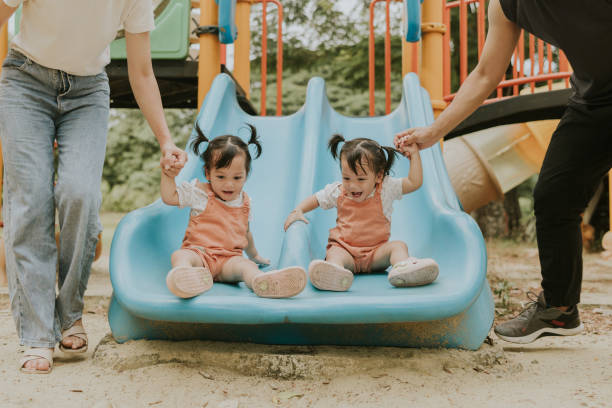 istock Double the Fun: excitement Twin Toddlers Enjoy the Slide with Parents 2201434255