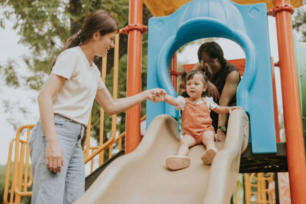 istock Asian mother helping hands, supported her kid to play sliding at playground. 2201434390