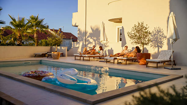 istock Young Diverse Couples Relaxing by the Pool at Sunset with Lush Palm Trees and Golden Light 2201435480