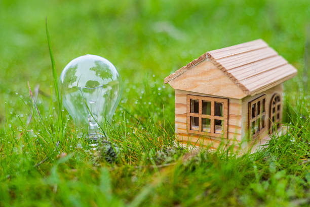istock Light bulb reflecting trees and a miniature wooden house sit on a patch of dewy grass, symbolizing the concept of eco-friendly housing and sustainable energy solutions for a greener future 2201437402