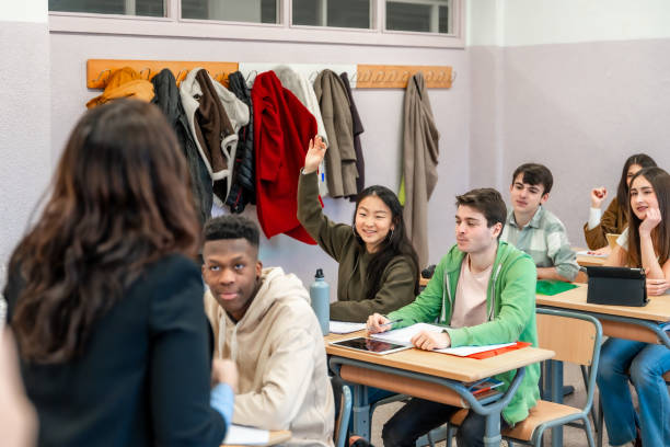 istock High school student raising hand to answer teacher question in classroom 2201440768