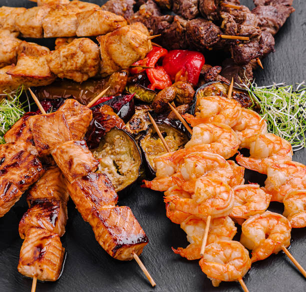 istock Grilled skewers featuring shrimp, beef, and chicken served on a slate platter with vegetables 2201442646