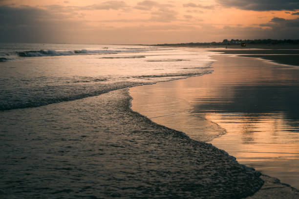 Waves gently washing ashore under a dramatic sunset sky with clouds.