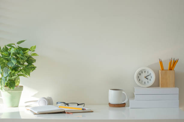 istock Bright desk setup with a potted plant, a clock, and writing essentials like pencils, an open notebook, and glasses. 2201451330