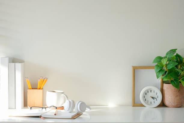 istock Desk setup includes an open notebook, glasses, a coffee mug, and headphones, complemented by a potted plant, a clock, and a pencil holder. 2201451341