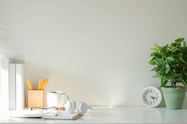 istock Simple work desk with a green plant, books and clock against white wall. 2201451561