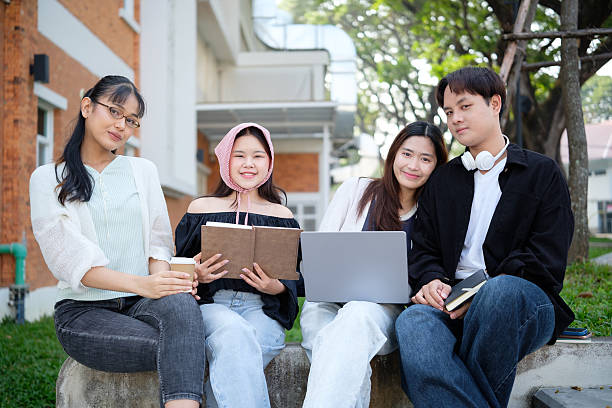 istock Group of students sitting on bench outside university building, sharing ideas and reviewing materials. Education concept. 2201451880