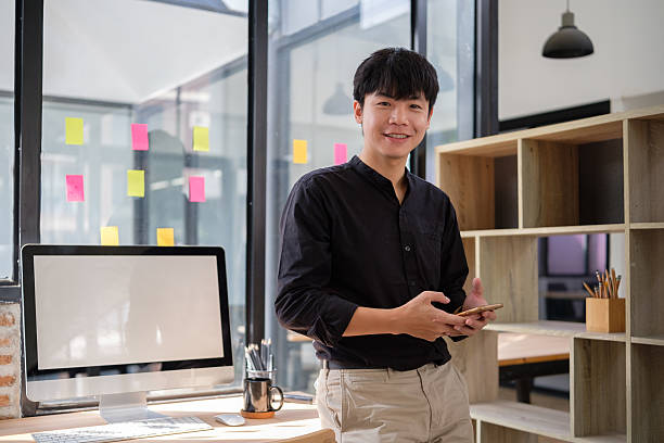 istock Confident businessman holding mobile phone standing in a modern office and smiling at camera. 2201452237