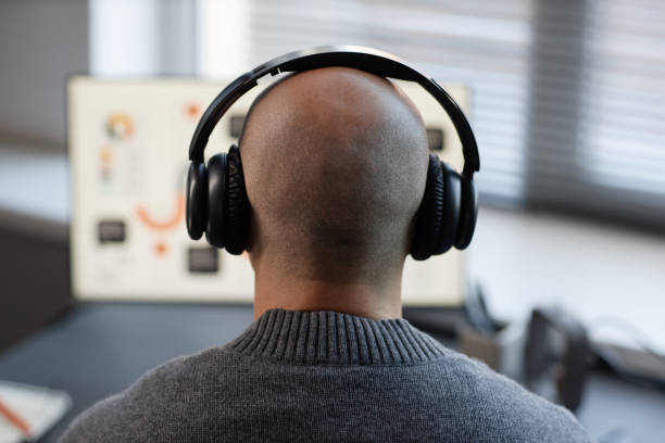 istock Bald Man Listening to Music Wearing Headphones while Using Computer in Office 2201460153