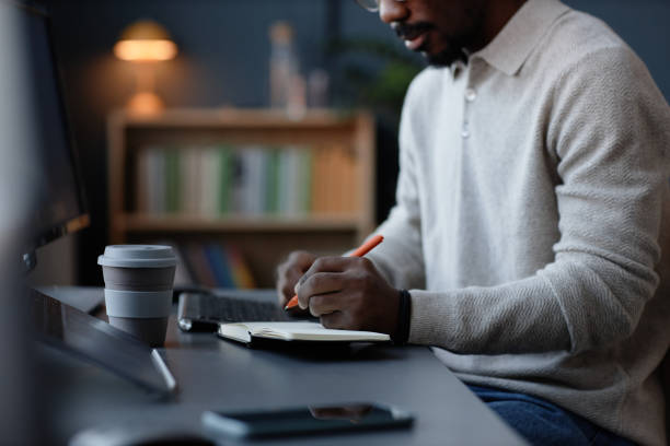 istock Black Male Corporate Employee Writing in Notebook while Planning Work in Office 2201460158
