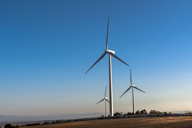 Three wind turbines stand tall on a rural hill in Catalonia, Spain, producing renewable energy under a clear blue sky during a summer afternoon.