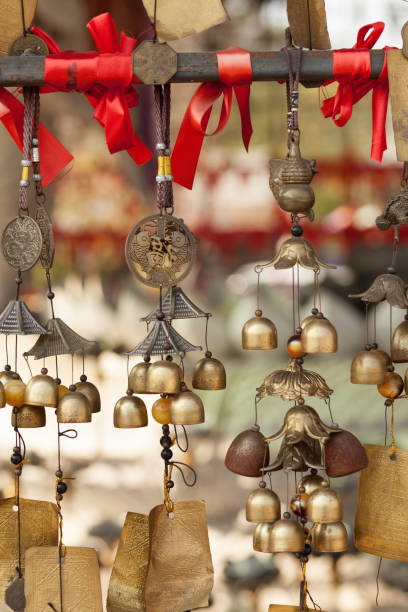 Close-up of wind chimes hanging from a wooden roof with copy space. The blurred background of lush green trees creates a peaceful, Zen-like outdoor atmosphere, perfect for relaxation and design use.