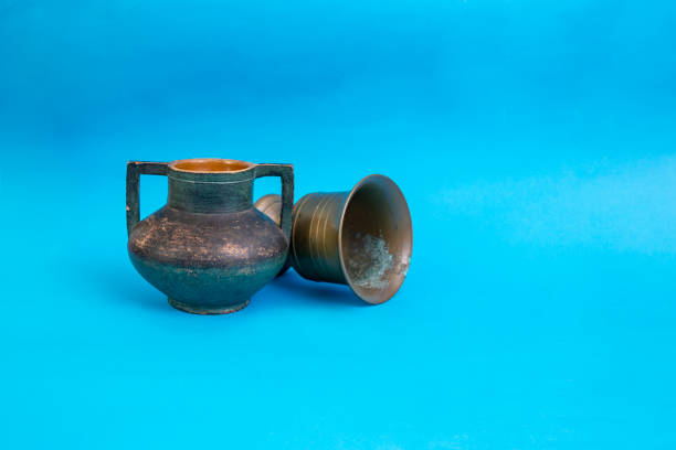 Ceramic vase and brass or copper mug, with textured patina, on blue  abstract backdrop