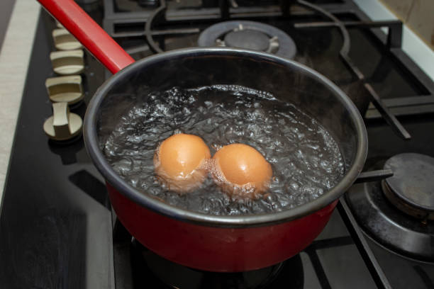 istock Two orange eggs boiling in a  black pot with bubbles and steam, soft focus  close up 2201473847