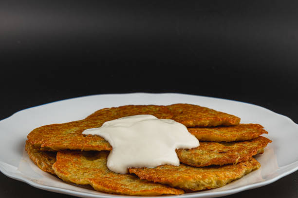 Golden brown potato pancakes arranged neatly on a white plate, topped with a generous dollop of creamy dipping sauce. Ideal for a hearty snack or appetizer, perfect for any gathering.