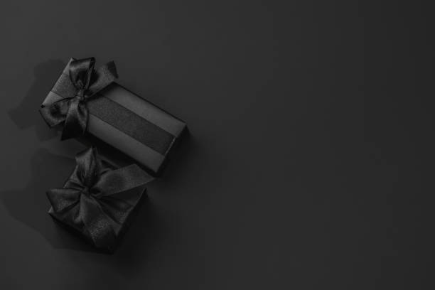 istock Two black gift boxes with satin bows on a dark black background with space for text. 2201479256