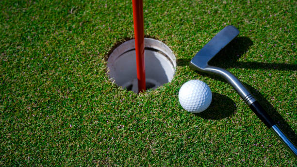 istock Top view of a golf ball with putter on green course at hole. 2201480402