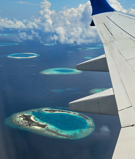 Airplane wing flying over an atoll in Maldives with turquoise water and white sand