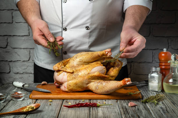 istock A skilled chef prepares a whole chicken for cooking, carefully adding fresh herbs and spices. The rustic kitchen setting enhances the culinary atmosphere, perfect for a delicious meal 2201483394