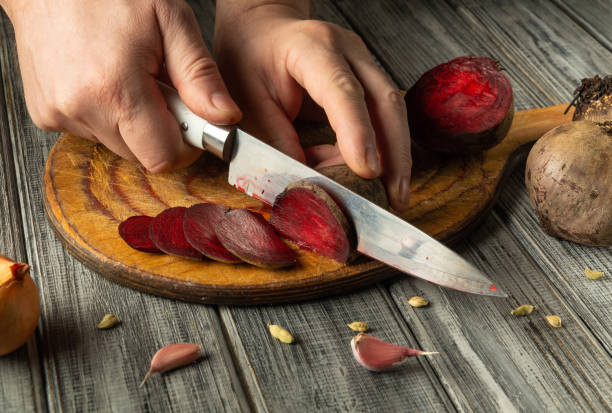 istock Hands expertly slice vibrant red beets on a rustic wooden board. Garlic and shallots are scattered in the background, showcasing a cozy cooking environment 2201483463