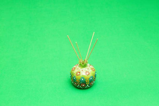 Green ceramic pomegranate shaped incense holder releasing fragrance on a vibrant green background, adding a touch of elegance and aroma