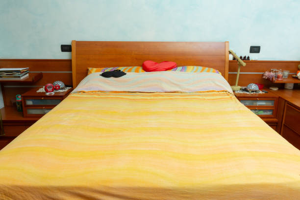 Unmade bed with a sleeping mask and a heart-shaped pillow suggests a restful night's sleep